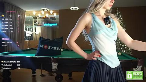 Media: Video of a young woman in a sleeveless top and pleated skirt, standing near a pool table in a modern room with a Christmas tree in the background.