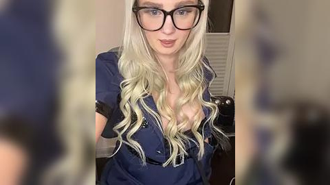 Media: A video of a fair-skinned, platinum blonde woman with long wavy hair, wearing black-rimmed glasses and a navy blue police uniform with a plunging neckline, revealing cleavage. Background features a white door and blurred figures.