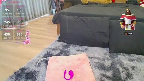 Media: A video captures a modern bedroom with a plush, gray shag rug, a pink vibrator, and a VR headset on the floor, with a plush toy and bed in the background.