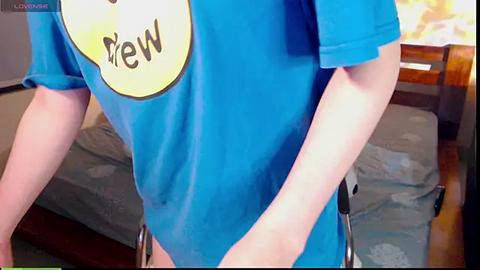 Media: A video of a person wearing a blue \"new\" t-shirt with a yellow smiley face logo, standing in a bedroom with a bed and wooden furniture.