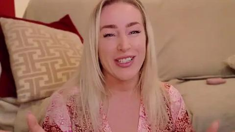Media: A video of a smiling, blonde woman with light skin and a pink lace top on a beige couch with patterned pillows.