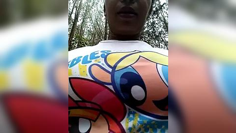 Media: A video of a woman wearing a white shirt with a cartoon character graphic, taken outdoors with blurred trees in the background.