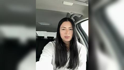 Media: Video of a young Asian woman with long black hair, wearing a white shirt, seated in the backseat of a car.