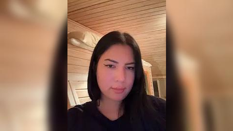 Media: A video of a young woman with long, straight black hair, wearing black clothing, standing in a cozy wooden sauna. The background features wooden walls and a soft, warm light.