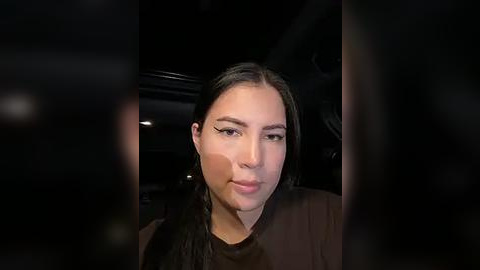 Media: Video of a woman with long black hair, fair skin, and light makeup, wearing a black top, looking out a car window at night.