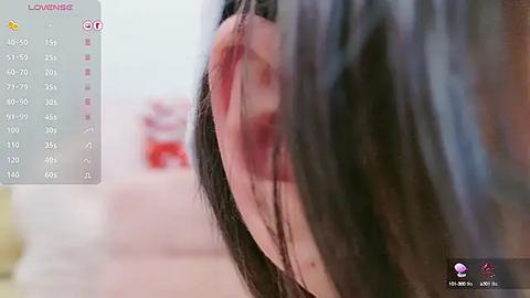 Media: Video of an Asian woman's injured ear, with blood seeping from a deep cut. The background is blurred, showing a light-colored room with a bed and a red object.