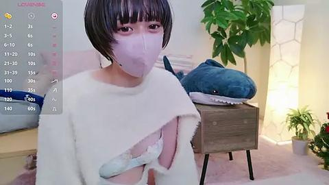 Media: A video of a young Asian woman with a short black bob, wearing a white face mask and a torn white sweater, sitting on a plush shark.