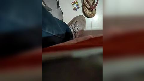 Media: A video captures a person's feet in brown sneakers, blue jeans, and a white t-shirt, lying on a tiled floor. A woven basket and colorful wall decorations are visible in the background.