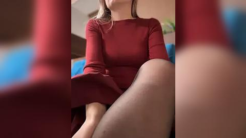 Media: A video of a woman in a red dress, sitting on a couch with blurred red and blue objects in the foreground, focusing on her legs and torso.