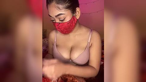 Media: A video of a woman with medium brown skin, wearing a red mask and pink bra, holding a plate of food. The background features a dimly lit room with pink lighting and string lights.