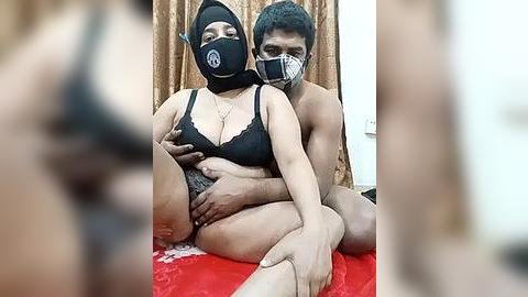 Media: Video of a dark-skinned woman in black lingerie and a mask, being held by a shirtless man in a red room.