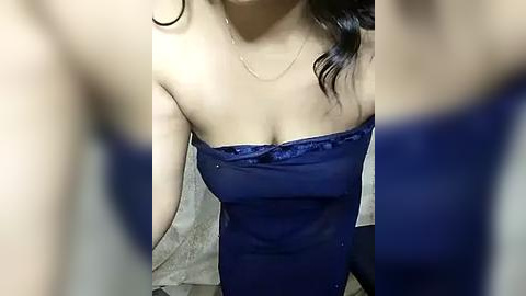 Media: A video of an Asian woman in a strapless, navy blue, sheer dress, revealing her cleavage, with wavy dark hair and a delicate gold necklace.