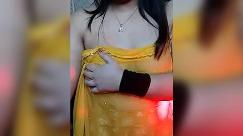 Media: A video of a woman with long black hair, wearing a yellow saree, holding her breasts, blurred background.