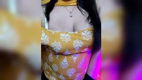 Media: A video of a woman with medium skin tone and long black hair, wearing a tight, mustard-yellow crop top with white floral patterns, revealing cleavage.