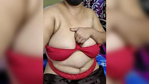 Media: Video of a plus-sized woman with light brown skin, wearing a red strapless bra and black shorts, adjusting her bra straps in a dimly lit room.