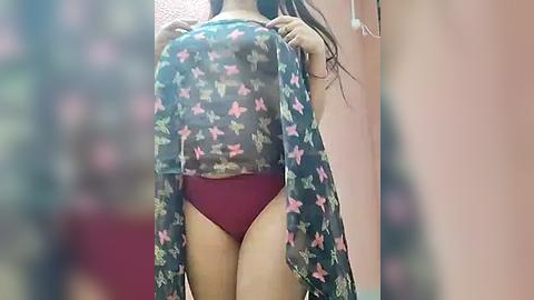 Media: Video of an Asian woman with long black hair, wearing a sheer, floral-patterned top and burgundy panties, standing in a dimly lit room with blurred background.