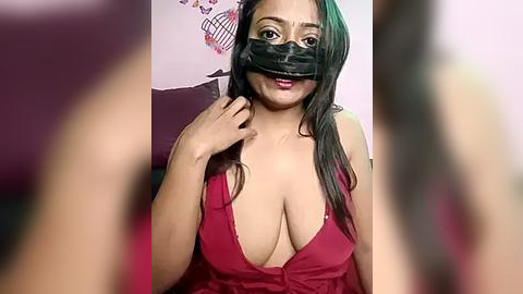 Media: Video of a young woman with long black hair, wearing a black mask, red dress with deep cleavage, and a playful expression. Background features a pink wall with abstract art.