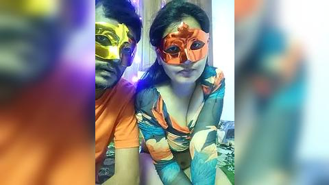 Media: Video of two people wearing vibrant, colorful masks with exaggerated features. The woman, with long black hair, has a floral dress. The man, with short black hair, wears an orange shirt. Background is blurred.