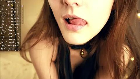 Media: Video of a young Asian woman with light skin and brown hair, licking her lips, wearing a black choker with a gold bell. Background shows a computer screen with chat window.