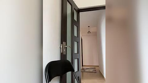 Media: Video of an open door with dark wooden panels, a black chair, and a hallway with light-colored walls, beige floor, and a ceiling light.