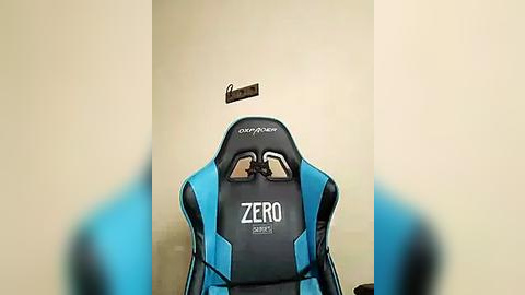 Media: Video of a blue and black gaming chair with the brand name \"Zero Gravity\" on the headrest, positioned in a minimalist room with beige walls and a small, dark hanging light fixture.