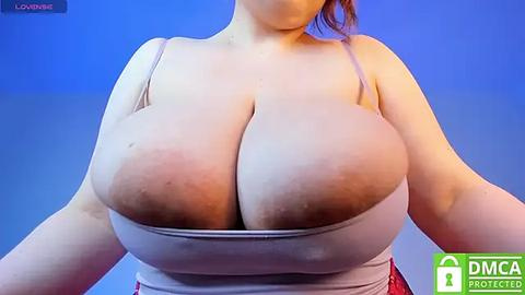 Media: Video of a fair-skinned woman with large, natural breasts, wearing a white tank top, against a blue gradient background. The image includes a watermark reading \"DMCA Protected.\