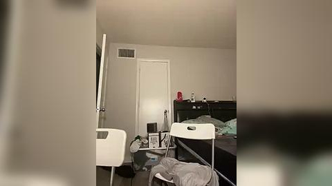 Media: Video of a cluttered, sparsely furnished dorm room with a white desk, chair, bed, and scattered clothes.