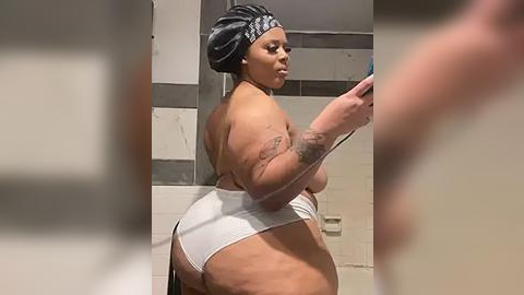 Media: Video of a plus-sized Black woman with a curvy figure, wearing a black headscarf and white thong, taking a selfie in a bathroom with beige tiles.