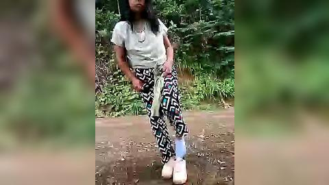 Media: A video of a young girl with long black hair, wearing a light gray shirt, black leggings with a geometric pattern, and white shoes, standing in a muddy, grassy outdoor area.