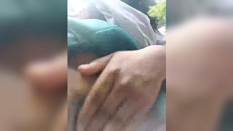 Media: A blurred video showing a person's hand holding a teal object against a blurred background, with indistinct greenery.