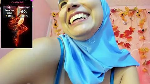 Media: Video of a smiling, fair-skinned woman with a blue hijab, surrounded by autumnal floral decorations.