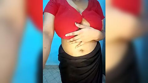 Media: Video of a light-skinned woman with large breasts, wearing a red crop top and black skirt, partially exposing her belly. Background shows a blue wall and tiled floor.