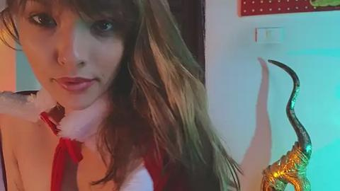 Media: Video of a young woman with long, wavy brown hair and fair skin, wearing a red and white Santa outfit, with a long, decorative tail. Background shows a festive, possibly Christmas-themed room.