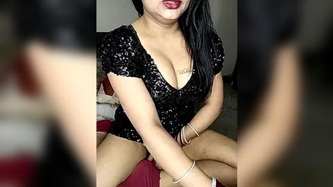 Media: Video of an Asian woman with long black hair, wearing a black sequin top, sitting on a red cushion.