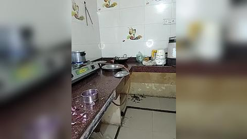 Media: A video shows a messy kitchen with a maroon countertop, white tiles, a stainless steel pot, a pan, and dishes scattered on the floor, suggesting a chaotic and unclean environment.