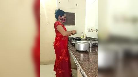 Media: Video of a woman in a red dress and face mask cooking on a kitchen counter, with a stainless steel pot and a stove.