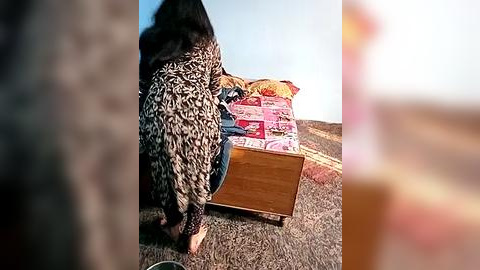 Media: Video of a person in a leopard-print dress pushing a wooden cart filled with colorful, patterned bags on a grassy hillside under a clear blue sky.