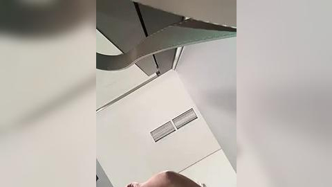 Media: Video of a modern, minimalist office ceiling with a light gray, textured surface and a white air vent. The angle is from the floor looking up, capturing the underside of a hanging light fixture.