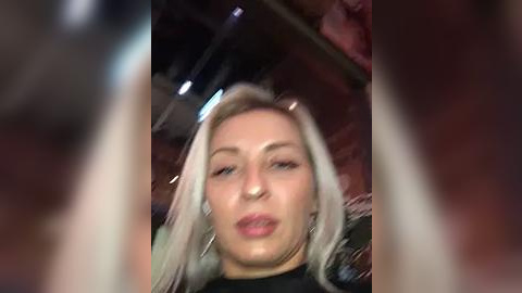 Media: Video of a young woman with platinum blonde hair, light skin, and full lips, puckering her lips, possibly in a nightclub setting.