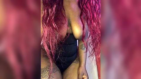 Media: A close-up video of a dark-skinned woman with long, wavy, bright pink hair, wearing a black, lacy bra, revealing her large breasts and tattoos on her thighs and arms.