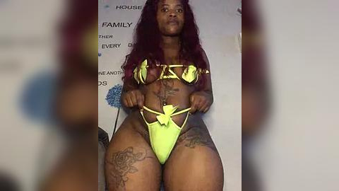 Media: Video of a voluptuous Black woman with long, curly red hair, wearing neon green lingerie, standing confidently in front of a blurred background.