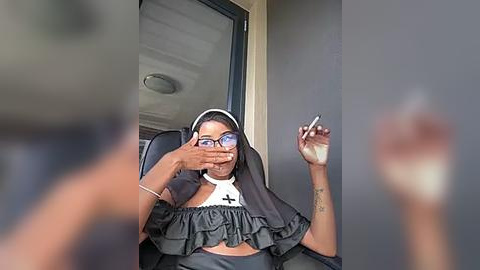 Media: A video of a dark-skinned woman wearing a black veil, glasses, and a revealing black top, smoking a cigarette, with a blurred figure in the background.