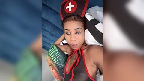 Media: A video of a young woman with light brown skin wearing a nurse costume, holding a green package, lying on a bed with blue walls and white sheets.