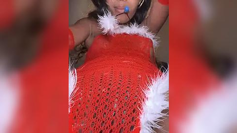 Media: A close-up video of a woman in a red, lacy, feathered bra, wearing a blue ball gag, with blurred red and white feathers in the foreground.