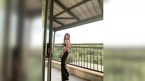 Media: A video of a woman with long, dark hair wearing a pink tank top and black pants, standing on a balcony with a green landscape background.