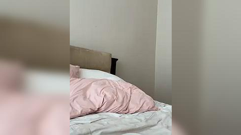 Media: A video of a messy, unmade bed with pale pink sheets and a beige headboard against a plain white wall, slightly blurred in the foreground.