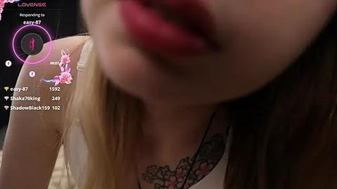 Media: A blurred video of a woman with long, blonde hair, wearing a low-cut top with floral designs, and bright red lipstick.