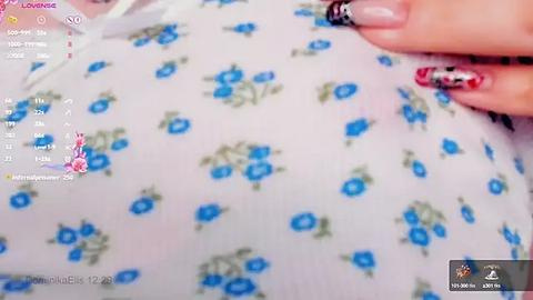 Media: A video of a woman's hand with manicured nails featuring a mix of red, black, and silver nail polish, resting on a white shirt with blue floral patterns. The shirt is slightly transparent.