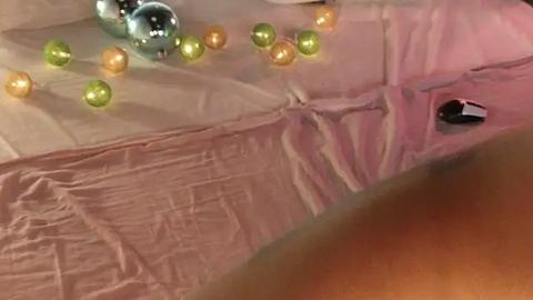 Media: Video of a person's hand holding a pink, crumpled piece of paper with a black eye visible through a tear. The hand is partially visible, with light skin and a few scattered gold and green beads.