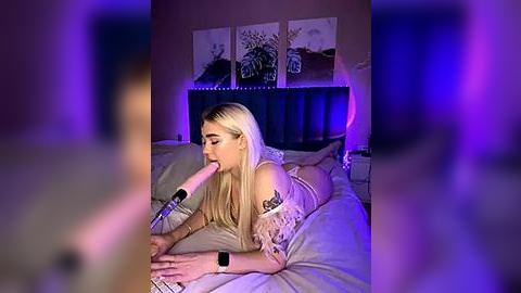 Media: Video of a blonde woman with fair skin, wearing a lace lingerie set, lying on a bed with a headboard, performing oral sex on a man, purple lighting in the background.